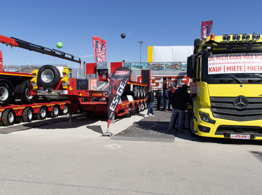 BAUMA 2025 Messestand der ES-GE. LKW von Mercedes-Benz mit Ladekran im Vordergrund. Weitere Satteltieflader und Auflieger.