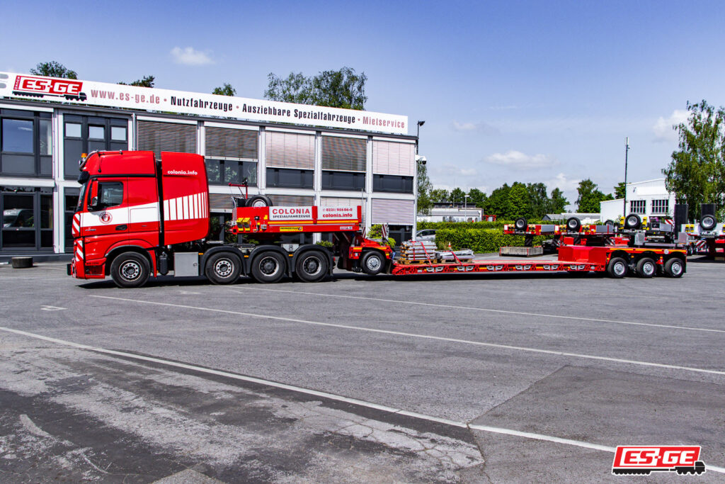 Mercedes-Benz Sattelzugmaschine von Colonia Spezialfahrzeuge mit 4 Achsen. Dahinter eine Tiefbettkombination des Typs Faymoville GigaMAX 1+3. Im Hintergrund das Gebäude der ES-GE.