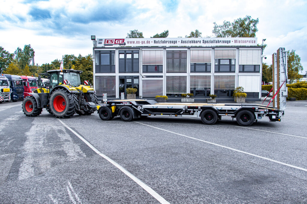 Ebert-Erdbau Claas Traktor mit 4-achsigem Tiefladeanhänger von Schwarzmüller hinter dem Gebäude der ES-GE, aufgenommen von der Fahrerseite