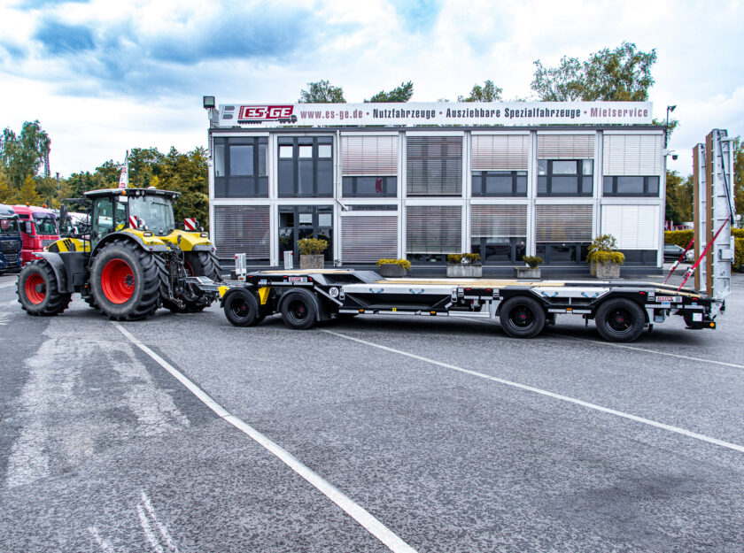 Ebert-Erdbau Claas Traktor mit 4-achsigem Tiefladeanhänger von Schwarzmüller hinter dem Gebäude der ES-GE, aufgenommen von der Fahrerseite