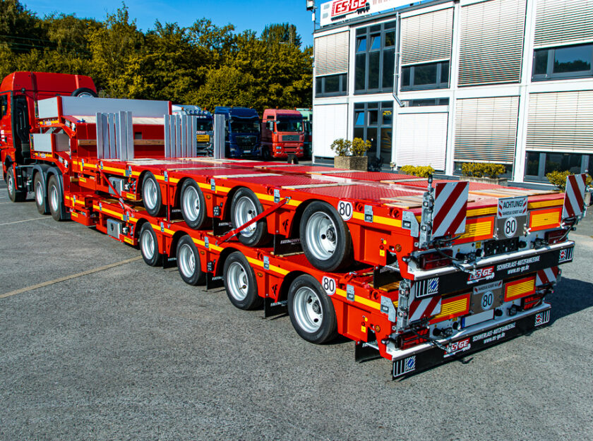 Sattelzugmaschine mit aufgesatteltem Faymonville MultiMAX mit vier Achsen. Auf der Ladefläche ein weiteres, identisches Fahrzeug. Seitlich von hinten aufgenommen hinter dem Hauptgebäude der ES-GE.