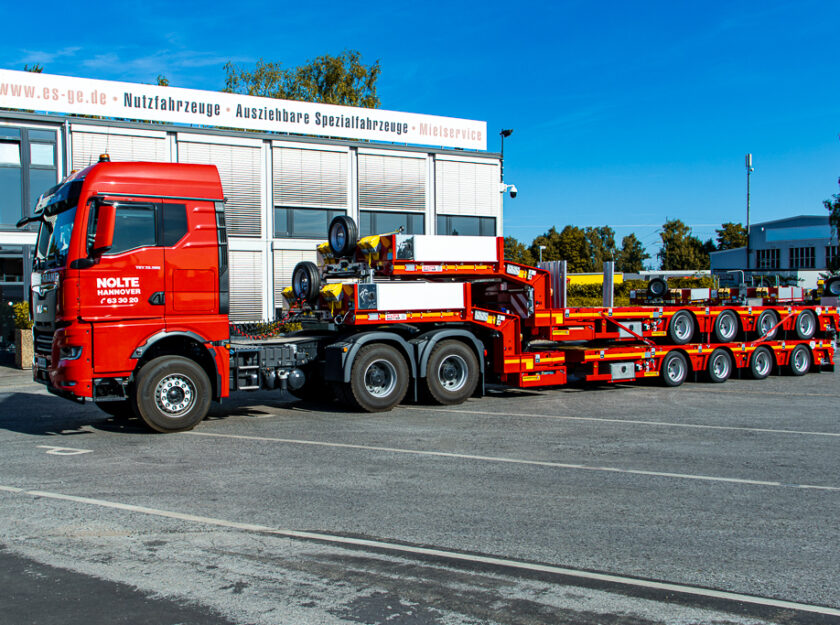 Sattelzugmaschine mit aufgesatteltem Faymonville MultiMAX mit vier Achsen. Auf der Ladefläche ein weiteres, identisches Fahrzeug. Seitlich von vorne aufgenommen hinter dem Hauptgebäude der ES-GE.