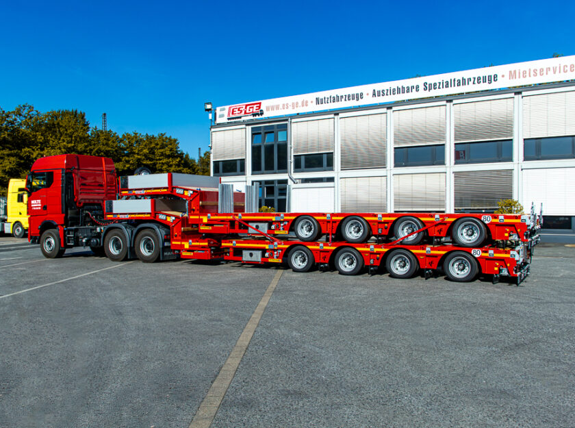 Sattelzugmaschine mit aufgesatteltem Faymonville MultiMAX mit vier Achsen. Auf der Ladefläche ein weiteres, identisches Fahrzeug. Seitliche Ansicht auf dem Gelände der ES-GE hinter dem Hauptgebäude.