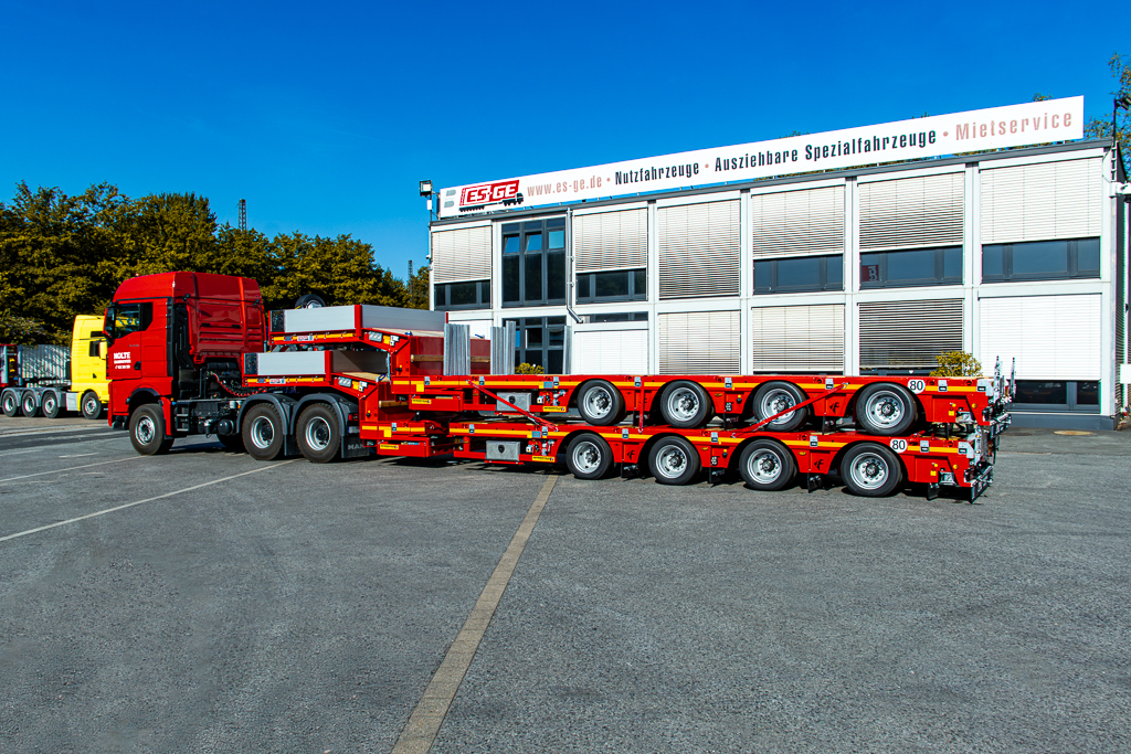 Sattelzugmaschine mit aufgesatteltem Faymonville MultiMAX mit vier Achsen. Auf der Ladefläche ein weiteres, identisches Fahrzeug. Seitliche Ansicht auf dem Gelände der ES-GE hinter dem Hauptgebäude.