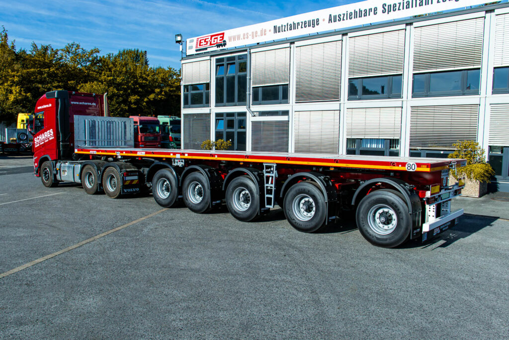 Sattelzugmaschine mit aufgesatteltem MAX Trailer MAX410 Ballastauflieger mit fünf Achsen, aufgenommen von links hinten. Der komplette Zug steht hinter dem Hauptgebäude der ES-GE.