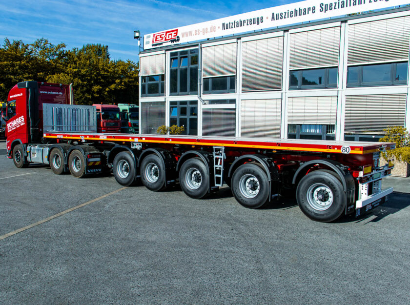 Sattelzugmaschine mit aufgesatteltem MAX Trailer MAX410 Ballastauflieger mit fünf Achsen,  aufgenommen von links hinten. Der komplette Zug steht hinter dem Hauptgebäude der ES-GE.